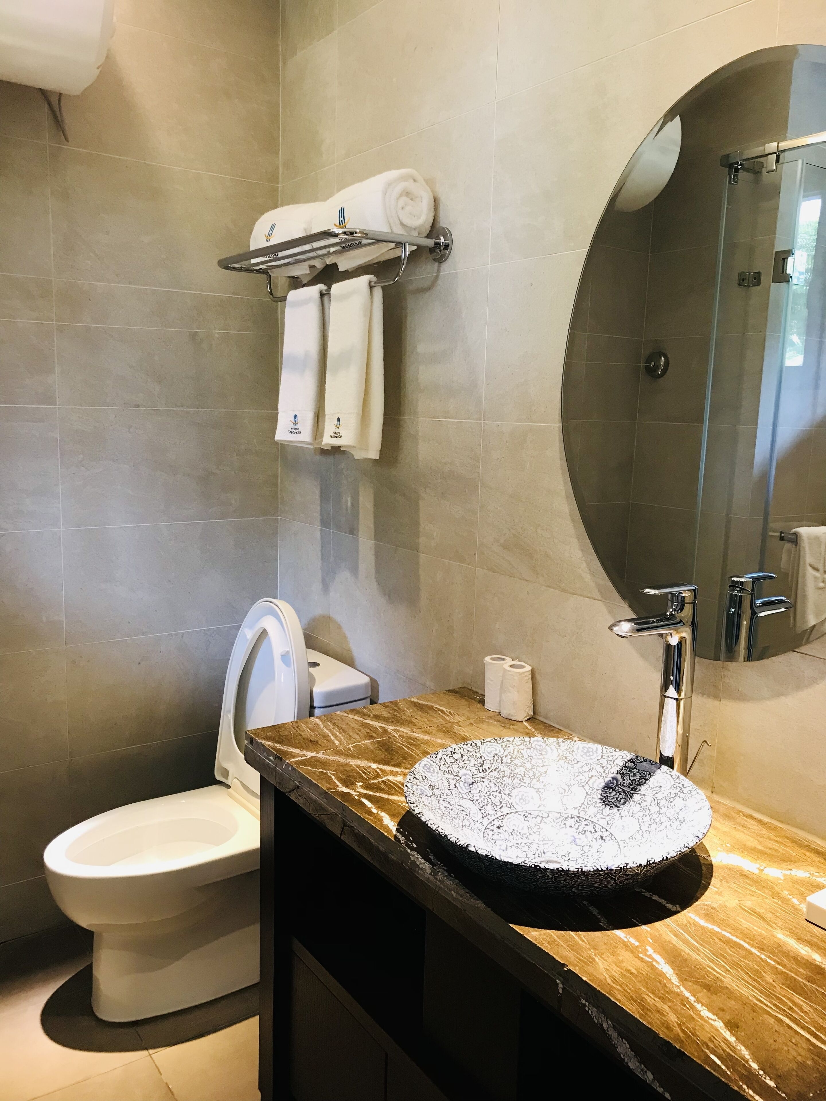 Ein modernes Badezimmer mit Marmorwaschbecken, Toilette, Handtuchhalter mit Handtüchern und einer Duschkabine aus Glas.