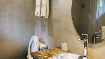 Ein modernes Badezimmer mit Marmorwaschbecken, Toilette, Handtuchhalter mit Handtüchern und einer Duschkabine aus Glas.