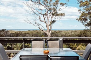 Relax in this serene outdoor seating area with a glass-top table and two comfortable chairs, surrounded by lush trees and a clear sky.