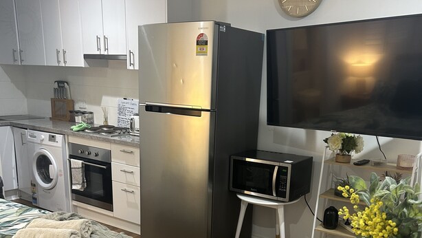 A compact kitchen with a refrigerator, microwave, and washing machine. There's a dining table with a basket and vase. - Pet friendly private studio, walking distance to lake  (Halekulani)