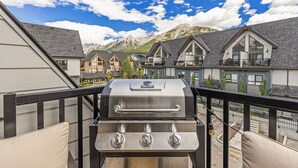 Un balcón con una parrilla de acero inoxidable, con vistas a una zona residencial con casas y montañas.