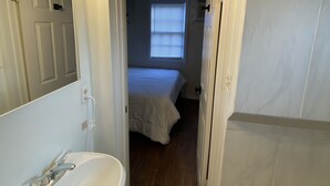 Un pasillo estrecho que conduce a un dormitorio con ventana, un baño con lavamanos y bañera, y un espejo con luces.