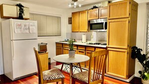 A compact kitchen with wooden cabinets, a refrigerator, a microwave, and a dining table with zebra-patterned chairs.