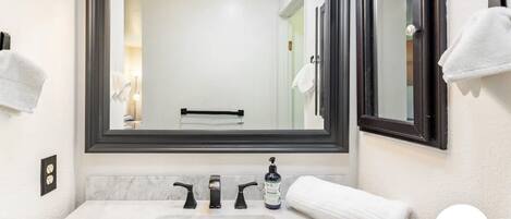 Een badkamer met een grote spiegel, een wit wastafelmeubel en een handdoekhouder.