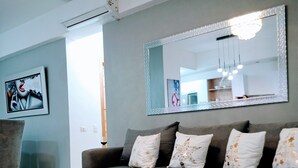 A modern living room with a grey sofa, a glass coffee table, and a large mirror above the sofa.