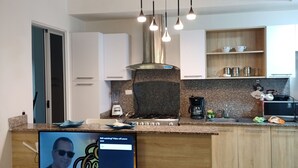 A modern kitchen with a built-in TV displaying a video, a stainless steel range hood, and a granite countertop.