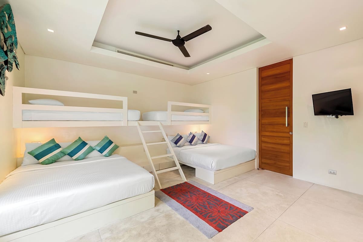 Ein kleines Zimmer mit Etagenbetten, Deckenventilator, Fernseher und Holztür.