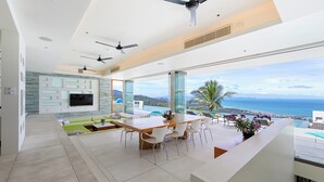 Ein modernes Wohnzimmer mit großem Essbereich, einem an der Wand befestigten Fernseher und Blick auf den Ozean.