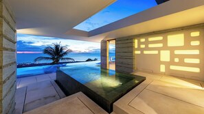 Un intérieur moderne avec une piscine, un palmier et une vue sur l’océan au crépuscule.