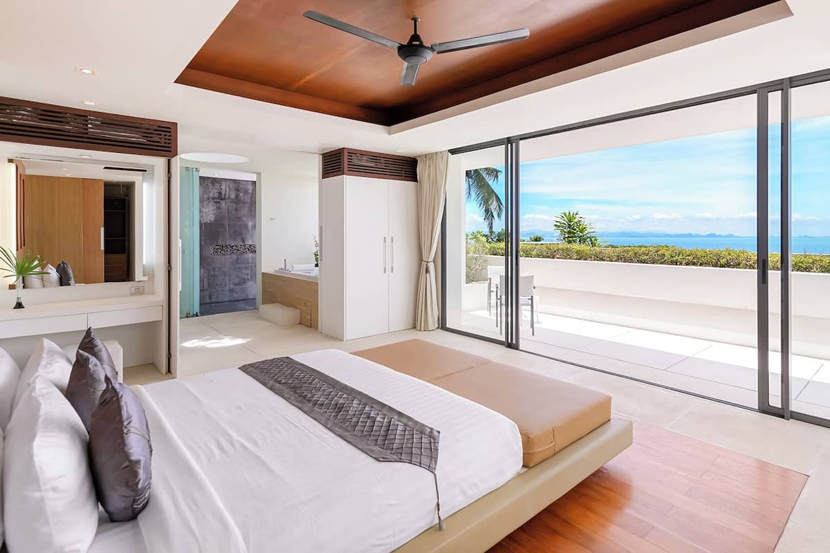 Ein modernes Schlafzimmer mit einem großen Bett, einem Deckenventilator und einem Balkon mit Meerblick.