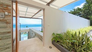 Ein modernes Interieur mit einer Glastür, die auf einen Balkon mit Blick auf einen Pool und das Meer führt.