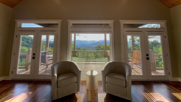 A spacious room with a high ceiling and wooden beams, featuring two large sliding glass doors that open to a balcony with a scenic mountain view. - Butterfly Mountain Cabin for 8 w/amazing view+wifi, 3 bdrm, 3.5 bath, & firepit (Franklin)