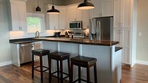 A modern kitchen with white cabinets, a stainless steel refrigerator, a microwave, and a coffee maker. There are three wooden stools at the island. - Butterfly Mountain Cabin for 8 w/amazing view+wifi, 3 bdrm, 3.5 bath, & firepit (Franklin)