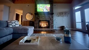 A living room with a stone fireplace, a large mirror, and a modern sofa. - Butterfly Mountain Cabin for 8 w/amazing view+wifi, 3 bdrm, 3.5 bath, & firepit (Franklin)