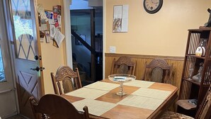 Un comedor con una mesa de madera, sillas, un reloj y una escalera al fondo.