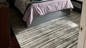 Un dormitorio con cama, mesita de noche, cómoda, ventana con persianas y estantes con objetos decorativos.