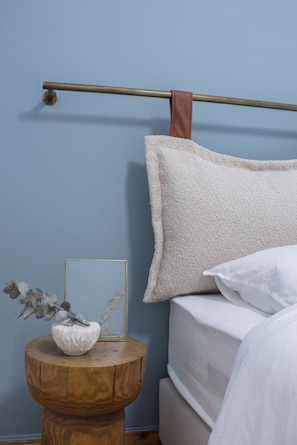 Ein Schlafzimmer mit einem Bett, einem Nachttisch aus Holz, einem gerahmten Bild und einem aufgehängten Handtuch.