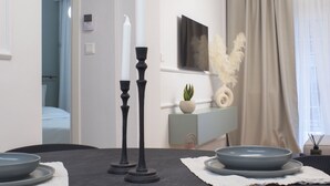 Un espace repas moderne avec une table sombre, deux bougies blanches et une décoration minimaliste comprenant une plante en pot et des plumes décoratives.