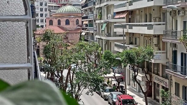 Une vue de rue avec des immeubles à plusieurs étages, des voitures garées et des arbres.