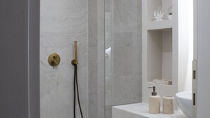 Une salle de bain moderne dotée d’une douche à parois de verre, d’un mur en marbre et d’un meuble-lavabo blanc avec un évier et des rangements.
