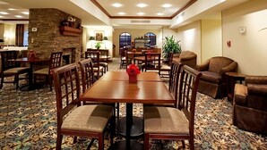 Een restaurant in een hotel, met een accentmuur van steen, houten tafels en stoelen, en een kamerbreed tapijt met een patroon.
