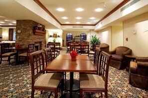 A hotel dining area with a stone accent wall, wooden tables and chairs, and a patterned carpet. - Spacious Accommodation w/ Full Kitchen Near Louisiana State University Campus! (Baton Rouge)