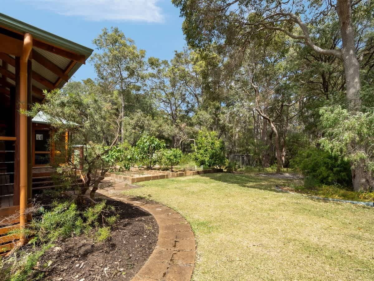 A residential property with a covered outdoor area, a curved pathway, and a variety of trees and shrubs.