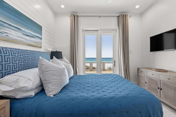 Un dormitorio con una cama grande, un televisor montado en la pared y vistas al mar a través de la ventana.