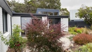 A modern house with a garage, a small garden with various plants, and a tree in the front yard. - This Pet Friendly property is the perfect escape to the beauty of Inverloch (Inverloch)