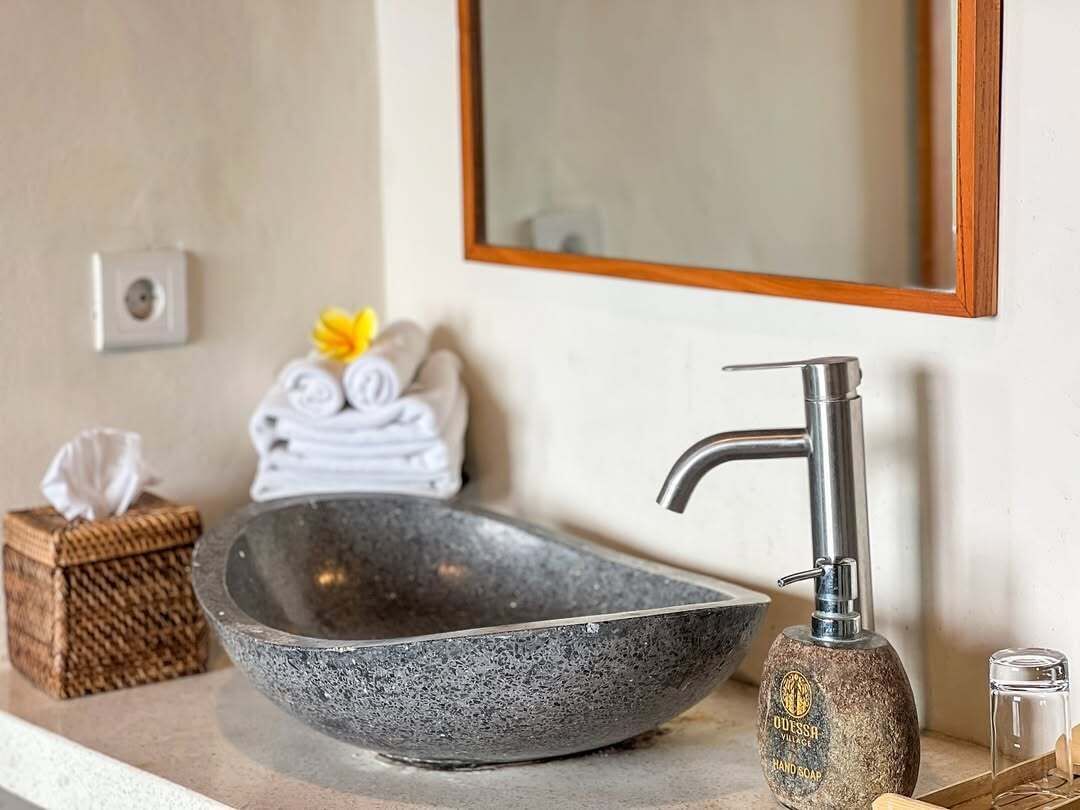 A bathroom with a stone basin, a modern faucet, a mirror, and a small wooden box.