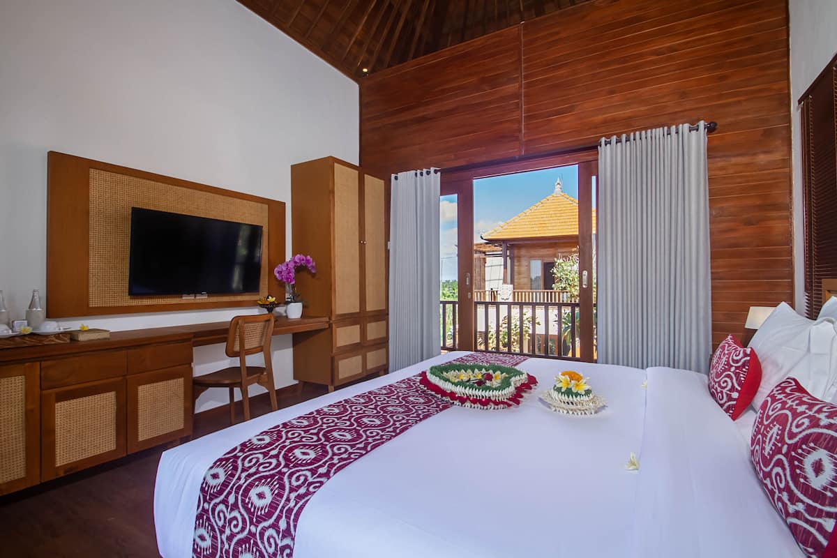 Habitación de hotel con una cama grande, un escritorio con televisión y un balcón con vista a un edificio.