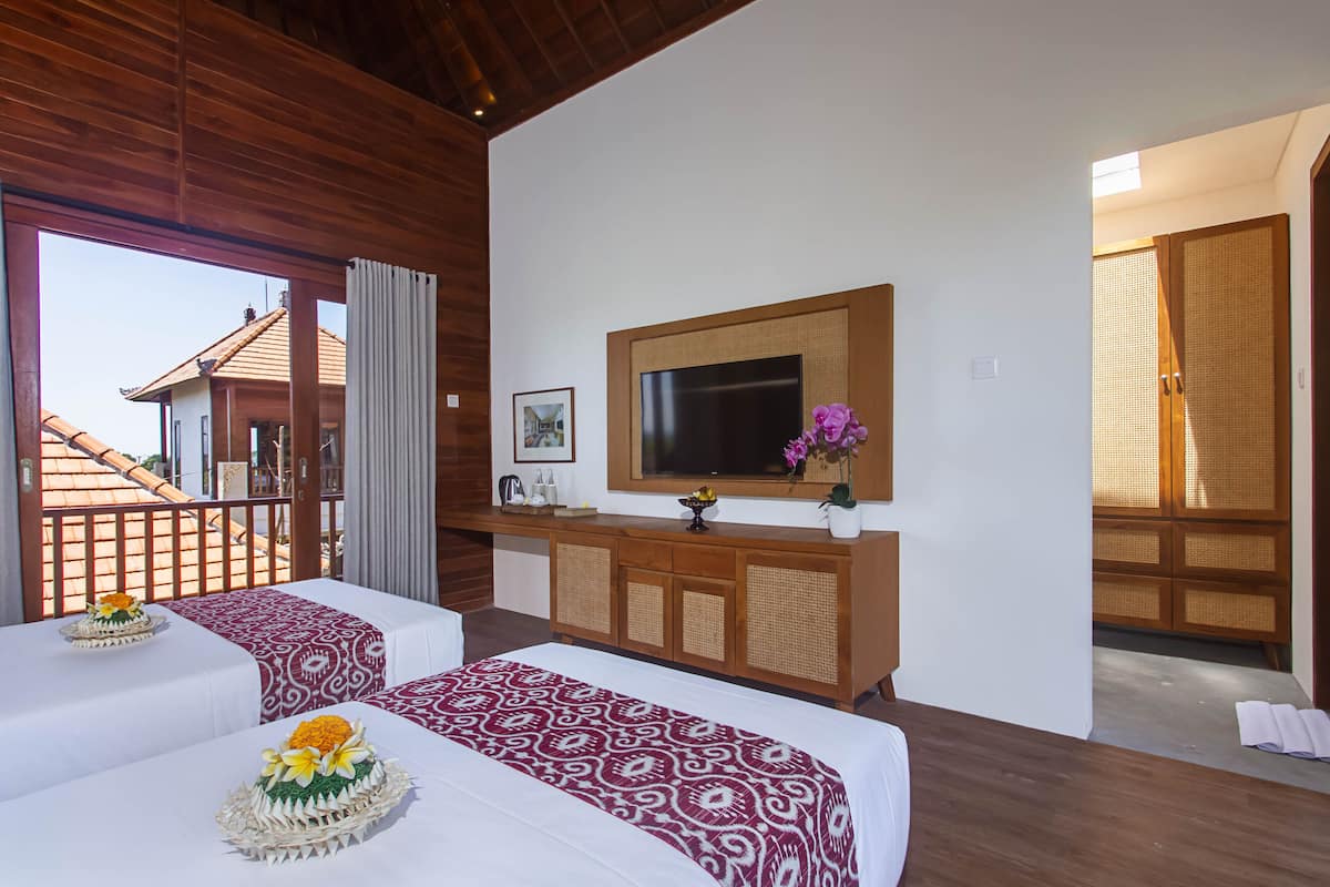 Habitación de hotel con dos camas, televisión, mueble de madera y balcón con vista a edificios.