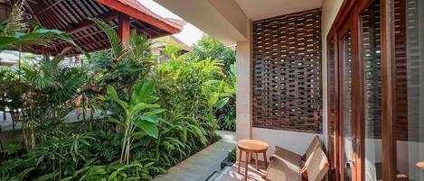 A balcony with a wooden floor, a small round table, two wicker chairs, and a wooden privacy screen.