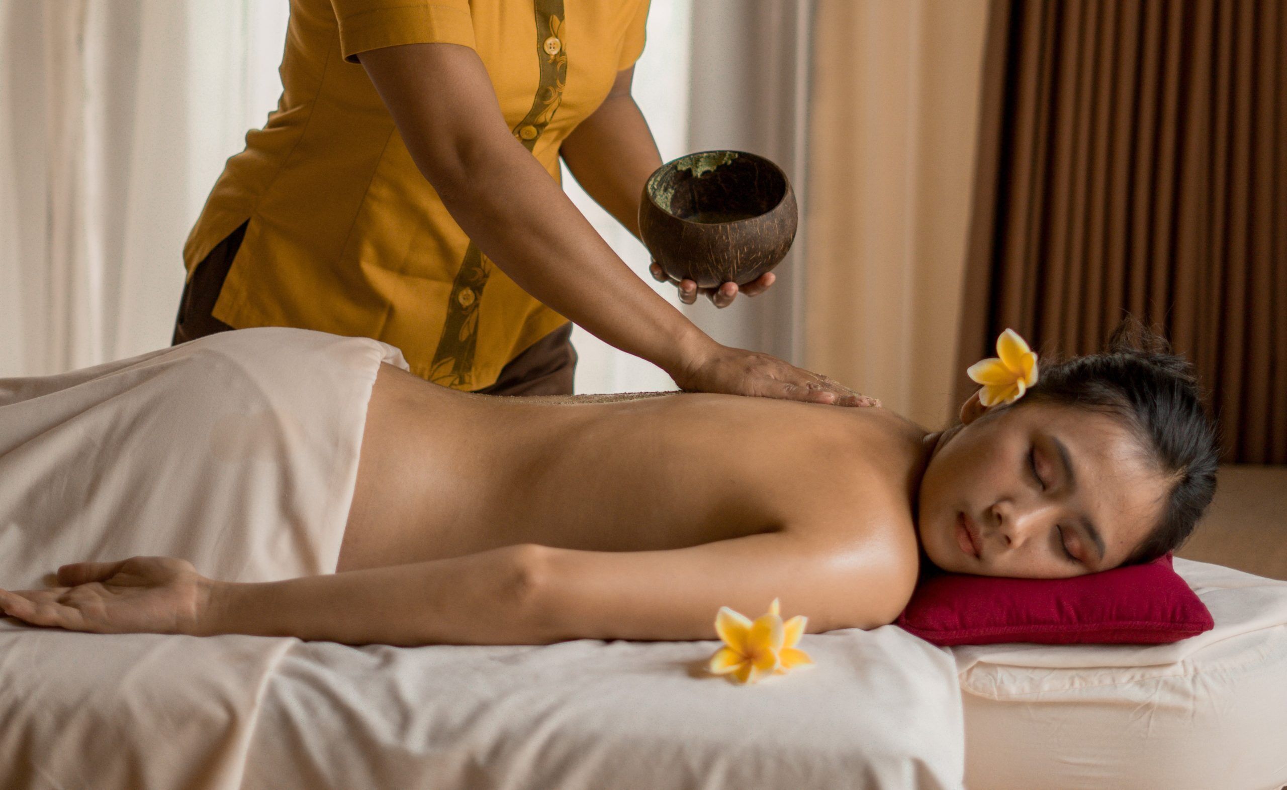 A person receiving a massage with a bowl and flowers on a bed.