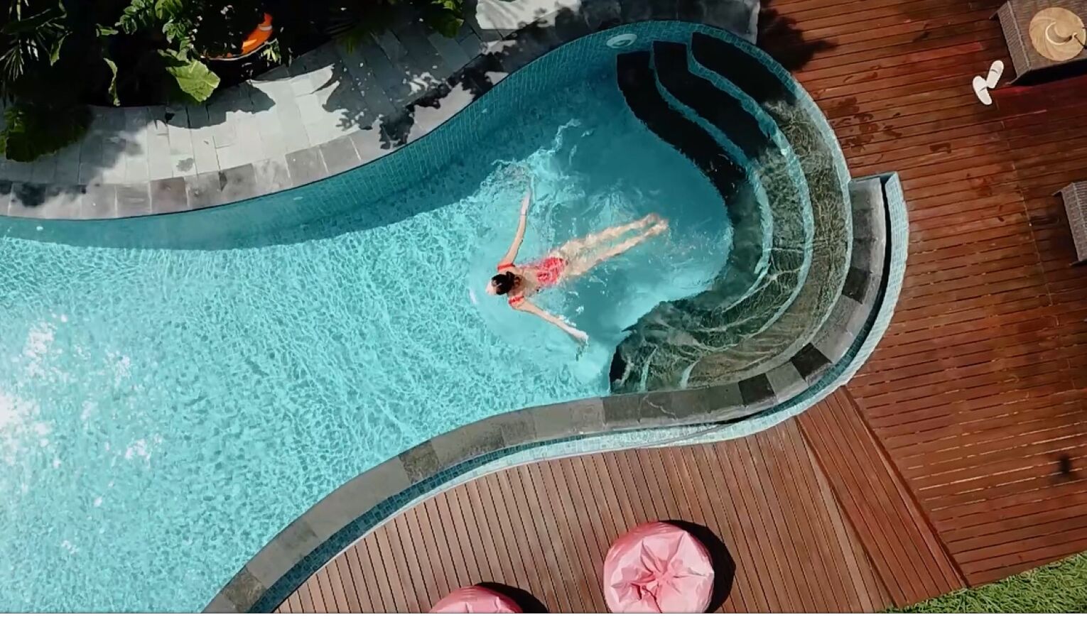 A person in a swimming pool with a curved edge and a wooden deck surrounding it.