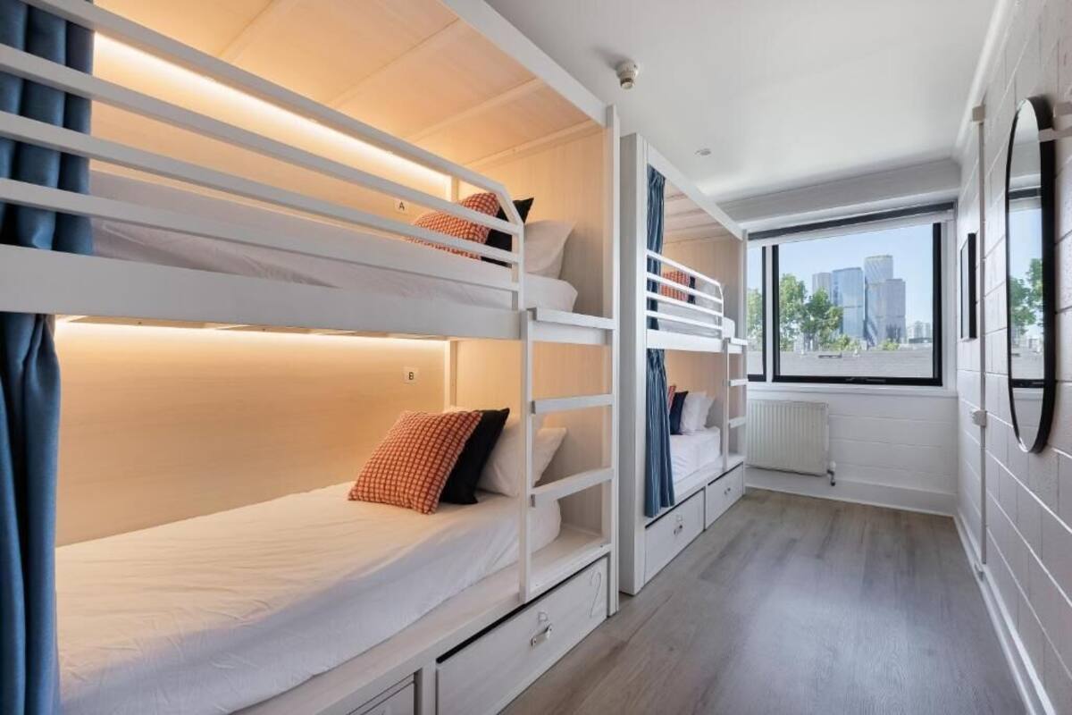 A modern hotel room with bunk beds, a view of the city, and a large window.