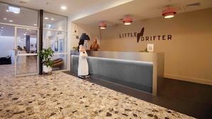 Una zona d'entrada amb sòl de marbre, un taulell de recepció i un cartell a la paret que diu "LITTLE DRIFTER".