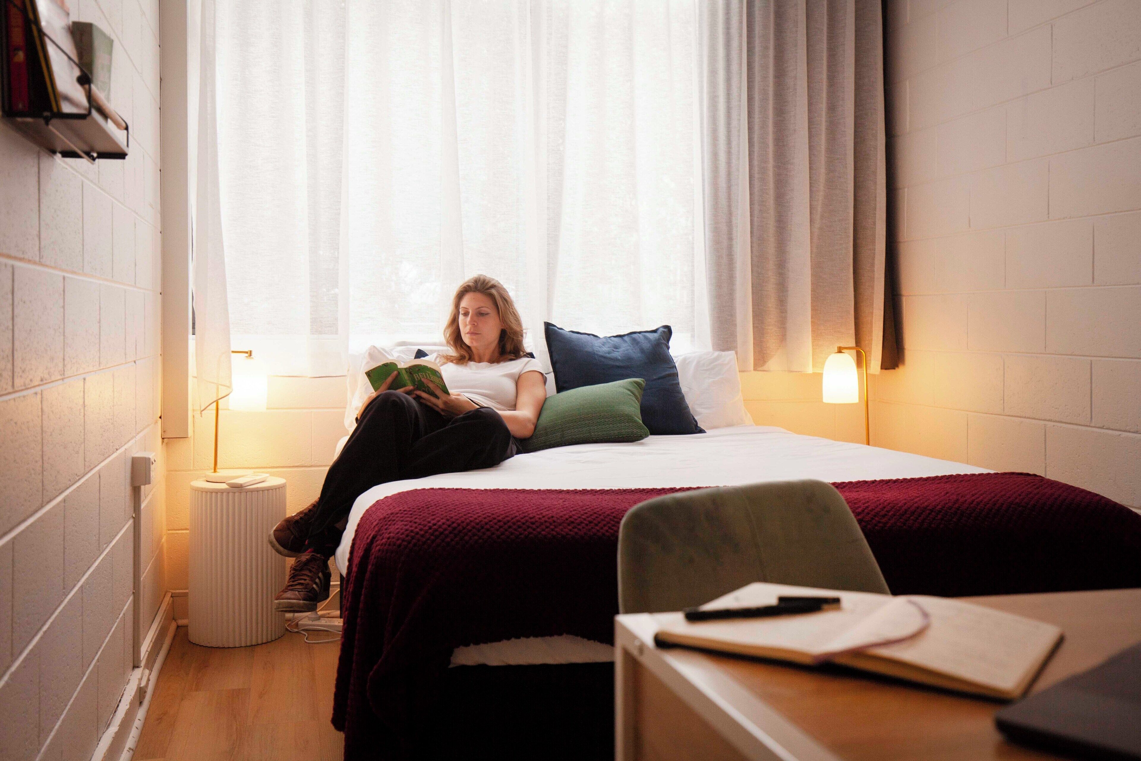 Une pièce comprenant un lit, une chaise, une table et une fenêtre avec des rideaux.