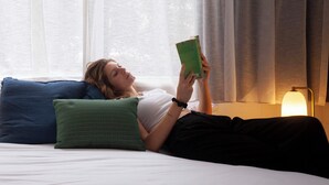 Una persona estesa en un llit amb coixins, llegint un llibre.