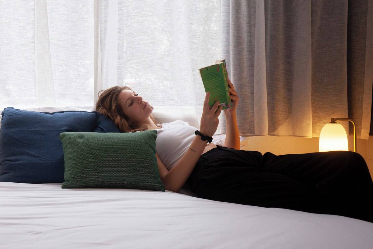 A person lying on a bed with pillows, reading a book.