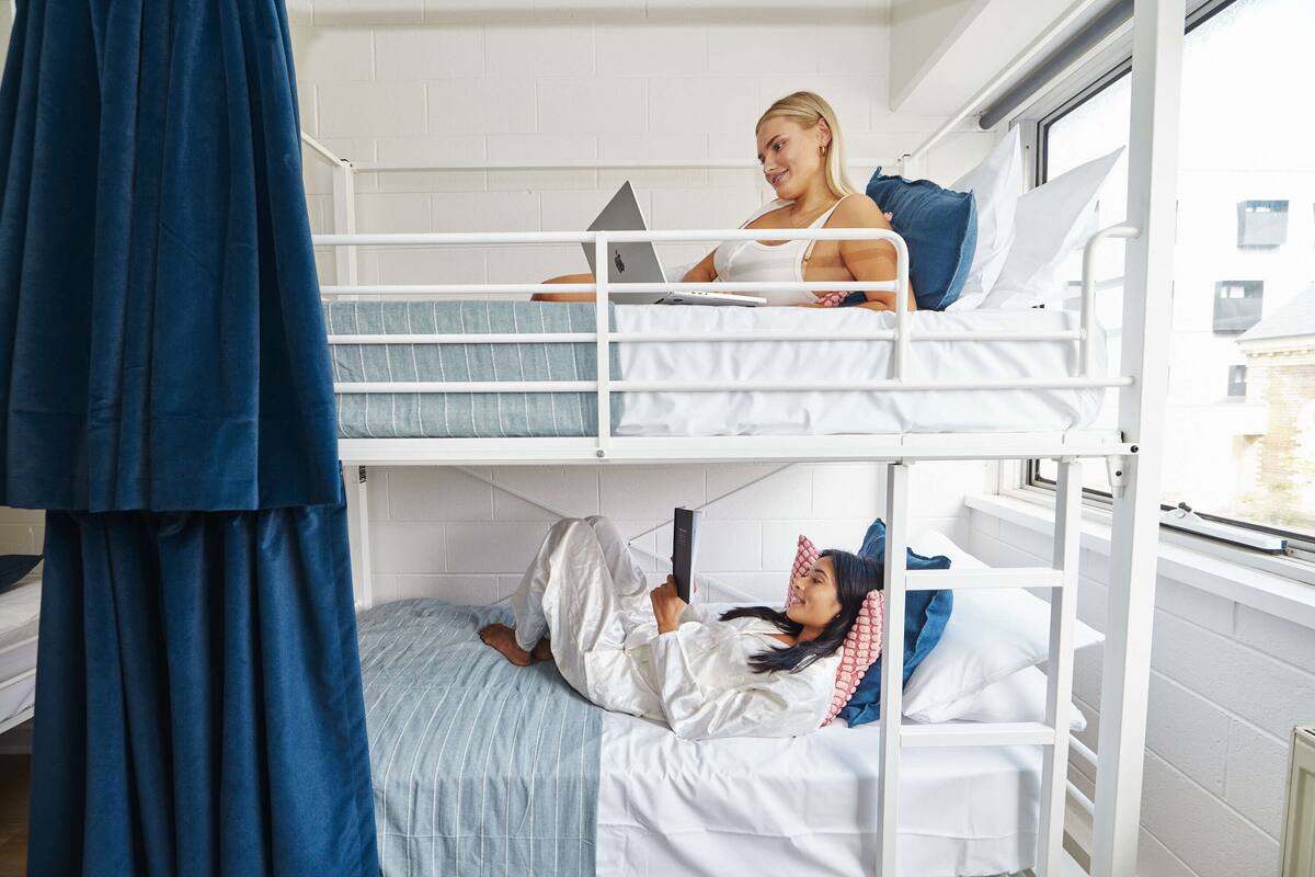 A bunk bed room with a laptop on the top bunk and a person lying on the bottom bunk.