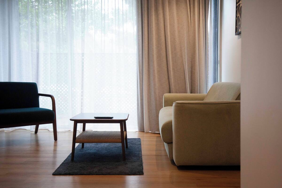 A living room with a dark green sofa, a beige sofa, a small wooden table, and a dark rug on a wooden floor.