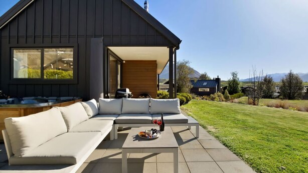 Una casa moderna con un amplio patio que incluye un sofá blanco y una mesa con una botella y aperitivos.