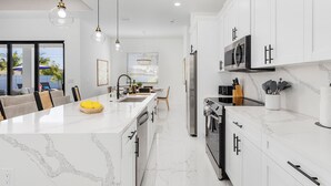 A modern kitchen with white cabinetry, a marble countertop, and stainless steel appliances. - Heated Saltwater I Pool Game Room | Firepit I BBQ (Cape Coral)
