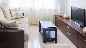 Un salon moderne avec un canapé, un pouf, une télévision et un meuble.