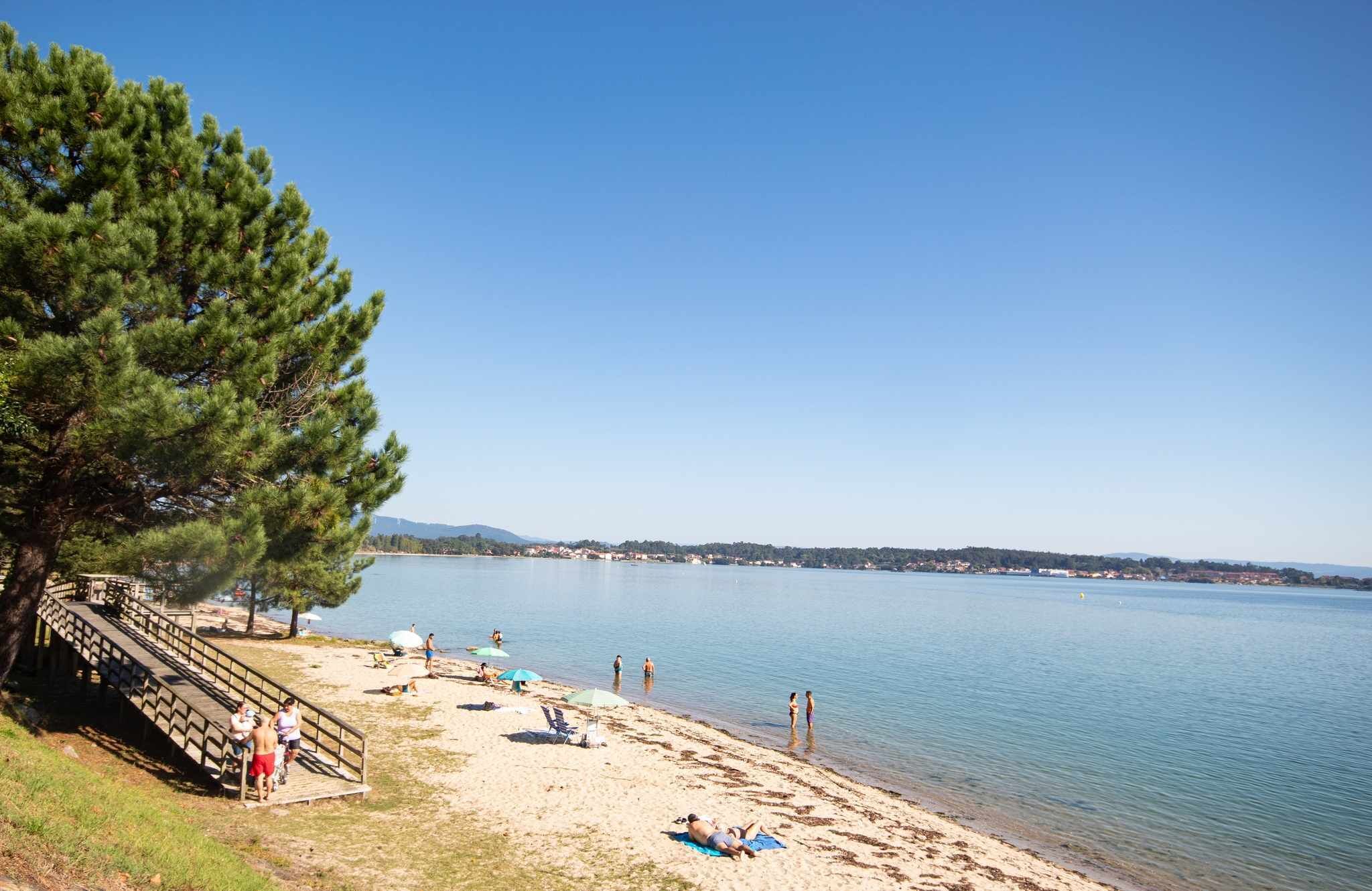 A beach with a wooden staircase leading down to the shore, a clear sky, and calm water.