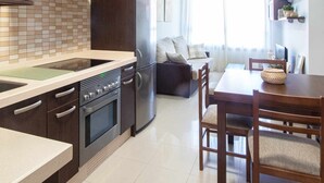 Une cuisine moderne avec des meubles de couleur sombre, un four encastré et un réfrigérateur. On y trouve également un coin repas avec une table et des chaises en bois.