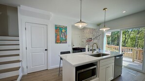 Une cuisine moderne dotée d’un îlot central, d’appareils électroménagers en acier inoxydable et de luminaires suspendus.