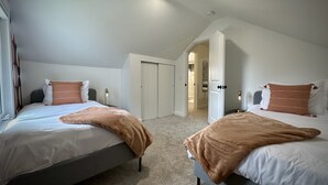 Une chambre avec deux lits, un dressing et une salle de bain visible par une porte ouverte.