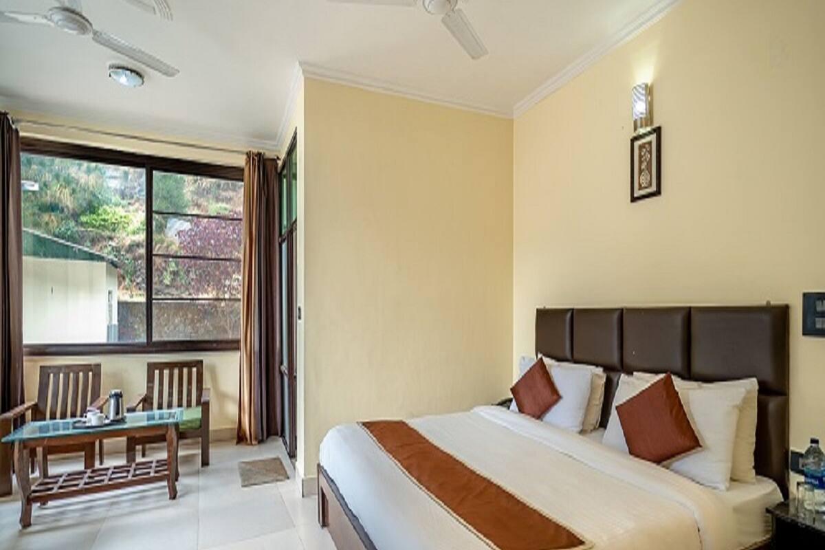 A hotel room with a large bed, two ceiling fans, a window with curtains, a wooden table with chairs, and a framed picture on the wall.